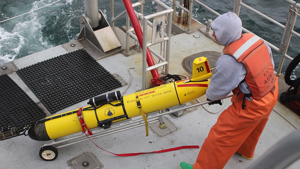 a person on the deck of a ship moves a torpedo-shaped object used for sound monitoring
