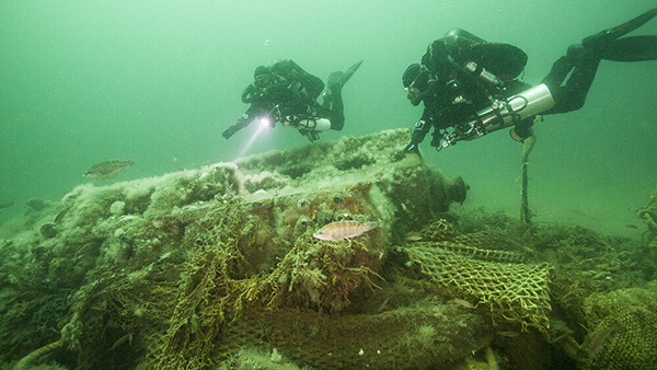 Two divers shine lights on a shipwreck