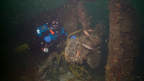 A diver grabs a propeller of a shipwreck and poses for a photo
