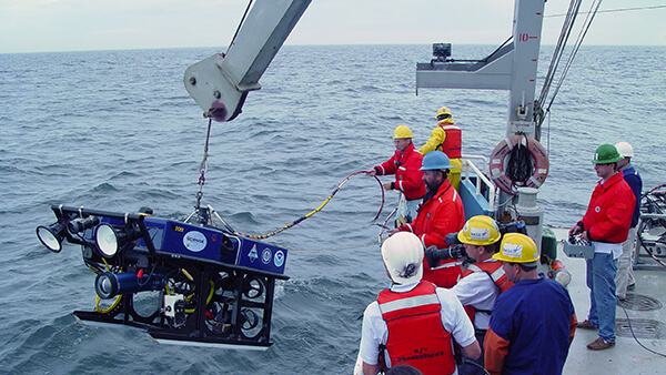 crew in orange vests work to launch an rov